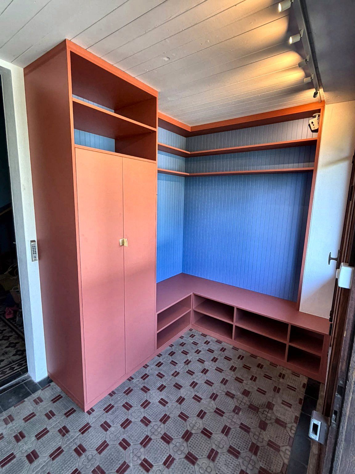 Aménagement d’angle sur mesure à Petit-Lancy : armoire corail, étagères et banc à casiers sur fond bleu