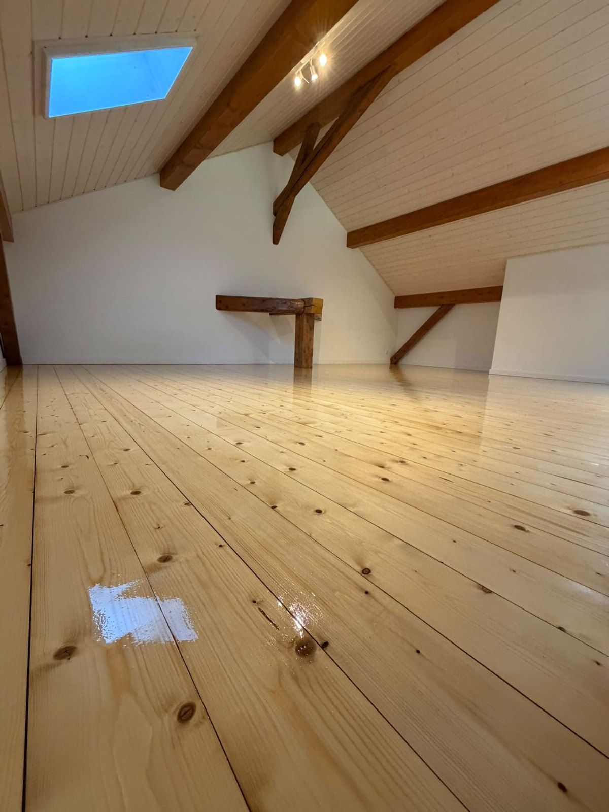 Plancher en bois clair terminé sous les combles, avec la charpente et les fenêtres de toit