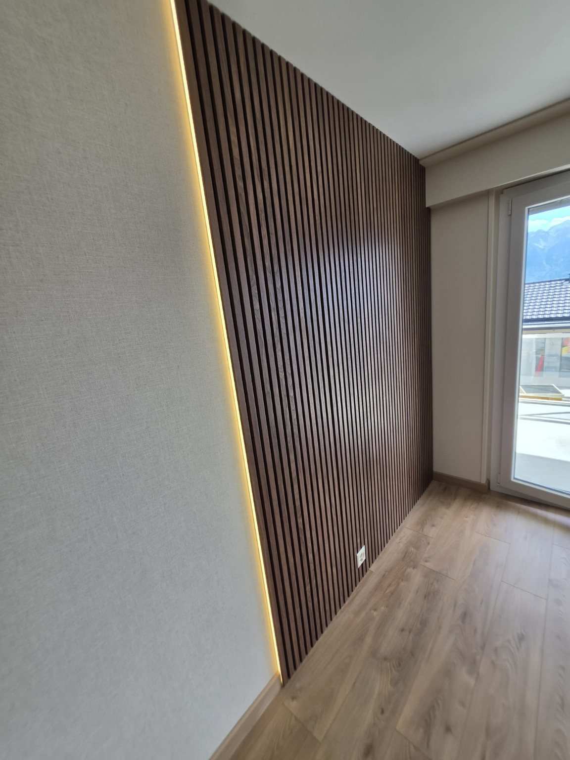 Habillage mural en tasseaux de bois avec éclairage LED indirect, dans l’appartement rénové à Vevey